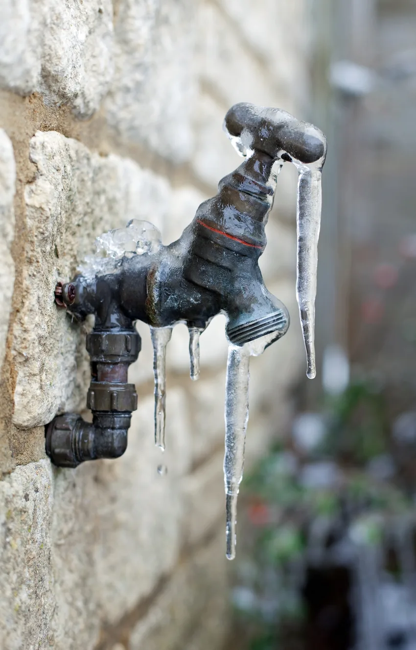 Outdoor faucet on a stone wall encased in ice with icicles hanging from the spout